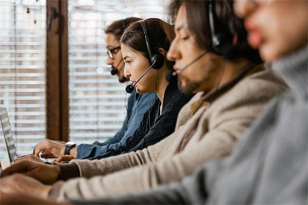 Callcenter Agents mit Headsets sitzen vor Laptops